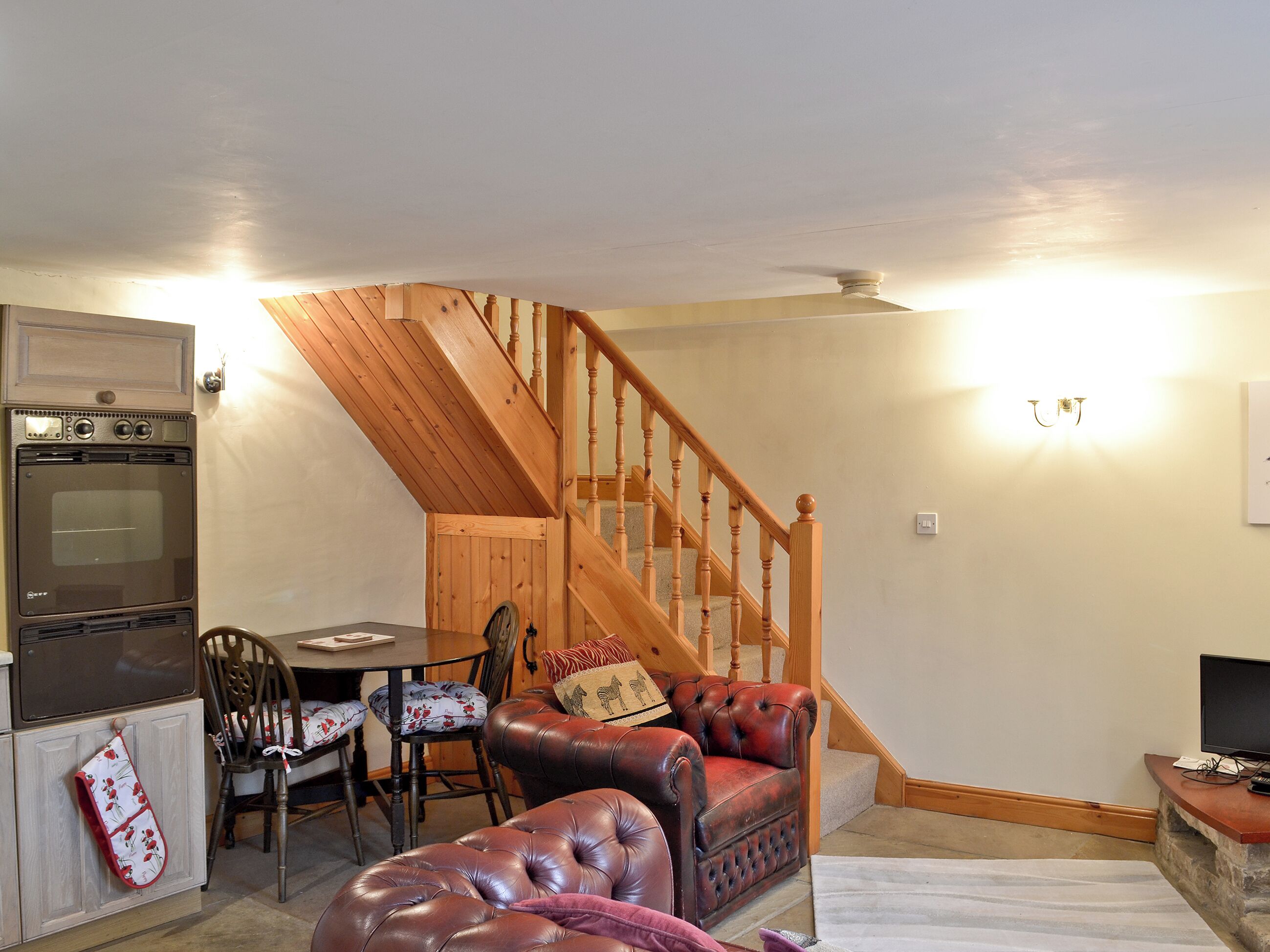 A cozy living room with a wooden staircase, a dining area, and a kitchen with a built-in oven.