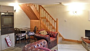 A cozy living room with a wooden staircase, a dining area, and a kitchen with a built-in oven. - 1 bedroom accommodation in Cromford, near Matlock (Cromford, near Matlock)