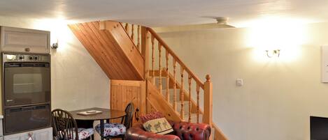 A cozy living room with a wooden staircase, a dining area, and a kitchen with a built-in oven.