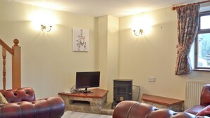 A living room with leather sofas, a stone fireplace, a television, and a staircase. - 1 bedroom accommodation in Cromford, near Matlock (Cromford, near Matlock)