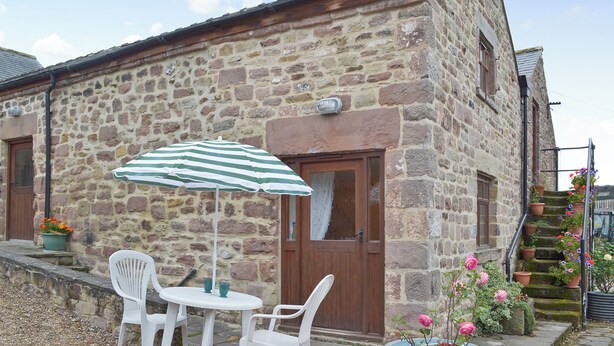 A stone building with a wooden door, a small table with two chairs, and a striped umbrella. - 1 bedroom accommodation in Cromford, near Matlock (Cromford, near Matlock)