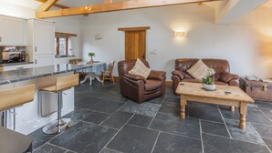 A spacious living area with a high ceiling and exposed wooden beams, a dining table with chairs, and leather sofas with cushions. - The Cart House - HNNH (Hartland)