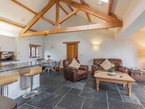 A spacious living area with a high ceiling and exposed wooden beams, a dining table with chairs, and leather sofas with cushions. - The Cart House - HNNH (Hartland)