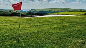 A golf course with a red flag, lush green grass, and rolling hills in the background. - The Cart House - HNNH (Hartland)
