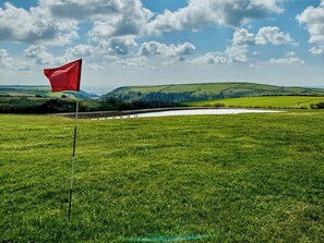 Ein Golfplatz mit einer roten Fahne, üppigem Grün und sanften Hügeln im Hintergrund.