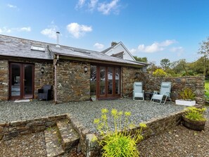 A stone building with a sloped roof, a large sliding glass door, and a small patio area with outdoor furniture. - The Cart House - HNNH (Hartland)