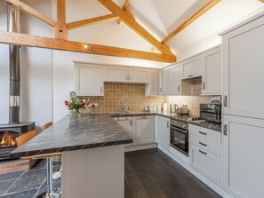 A modern kitchen with white cabinets, a marble countertop, a built-in oven, and a wood-burning stove.