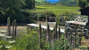 A garden with stone structures and a view of the sea. - The Cart House - HNNH (Hartland)