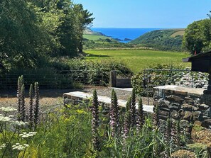 A rural landscape with a stone wall, a metal gate, and a view of the sea. - The Cart House - HNNH (Hartland)