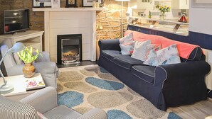 Una sala de estar acogedora con una pared de piedra, una chimenea, un sofá con cojines estampados, un sillón a rayas y un televisor.