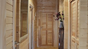 Ein Holzbodenkorridor mit einer Tür am Ende, einem Teppich auf dem Boden und einer Vase mit Blumen auf einem Regal.