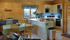 Eine gemütliche, rustikale Küche im Blockhausstil mit Holzwänden, einem Essbereich mit Tisch und Stühlen sowie einer kleinen Kücheninsel mit Spüle und Mülleimer.