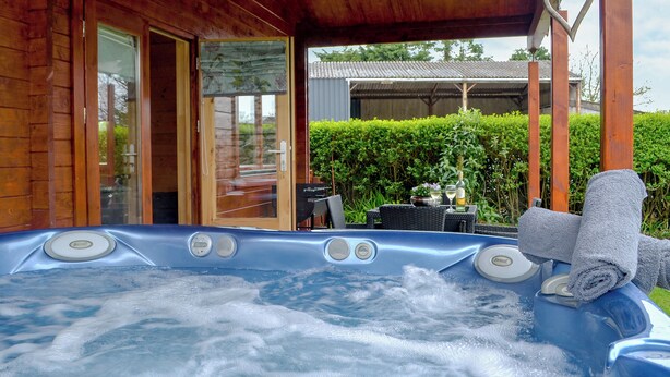 Ein Whirlpool in einer Holzhütte mit einer Glastür, die zu einer Terrassenanlage führt.