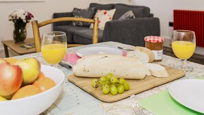 Et spisebord med frugt, brød og drikkevarer i en stue med sofa og radiator.