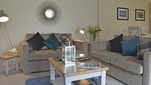 Un salon avec deux canapés, une table basse, une lampe, un vase avec des fleurs et des tableaux encadrés accrochés au mur.