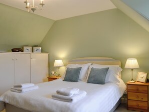 Ein ordentlich bezogenes Bett mit Kissen und gefalteten Handtüchern, eine Nachttischlampe und ein Nachttisch aus Holz mit einem Bilderrahmen.