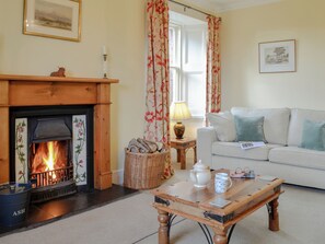 A cozy living room with a fireplace, a sofa, a coffee table, and a window with floral curtains. - Islabank Farmhouse - SAAP (Meigle)