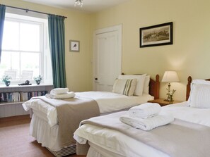 A hotel room with two beds, a window with curtains, a door, a framed picture on the wall, and a bedside table with a lamp and flowers. - Islabank Farmhouse - SAAP (Meigle)