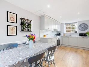 A modern kitchen with white cabinets, a dining table with a penguin-themed tablecloth, and a clock on the wall.