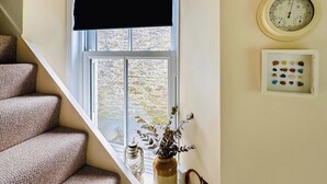 A staircase with a textured fabric wall, a window with a black blind, a wall clock, a thermometer, and a decorative jar with a plant. - 3 bedroom accommodation in Gorran Haven (Gorran Haven)