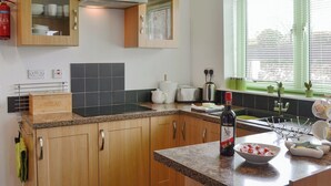 Une cuisine moderne avec des meubles en bois, une hotte de cuisine en acier inoxydable, un grille-pain encastré et une fenêtre avec des stores.