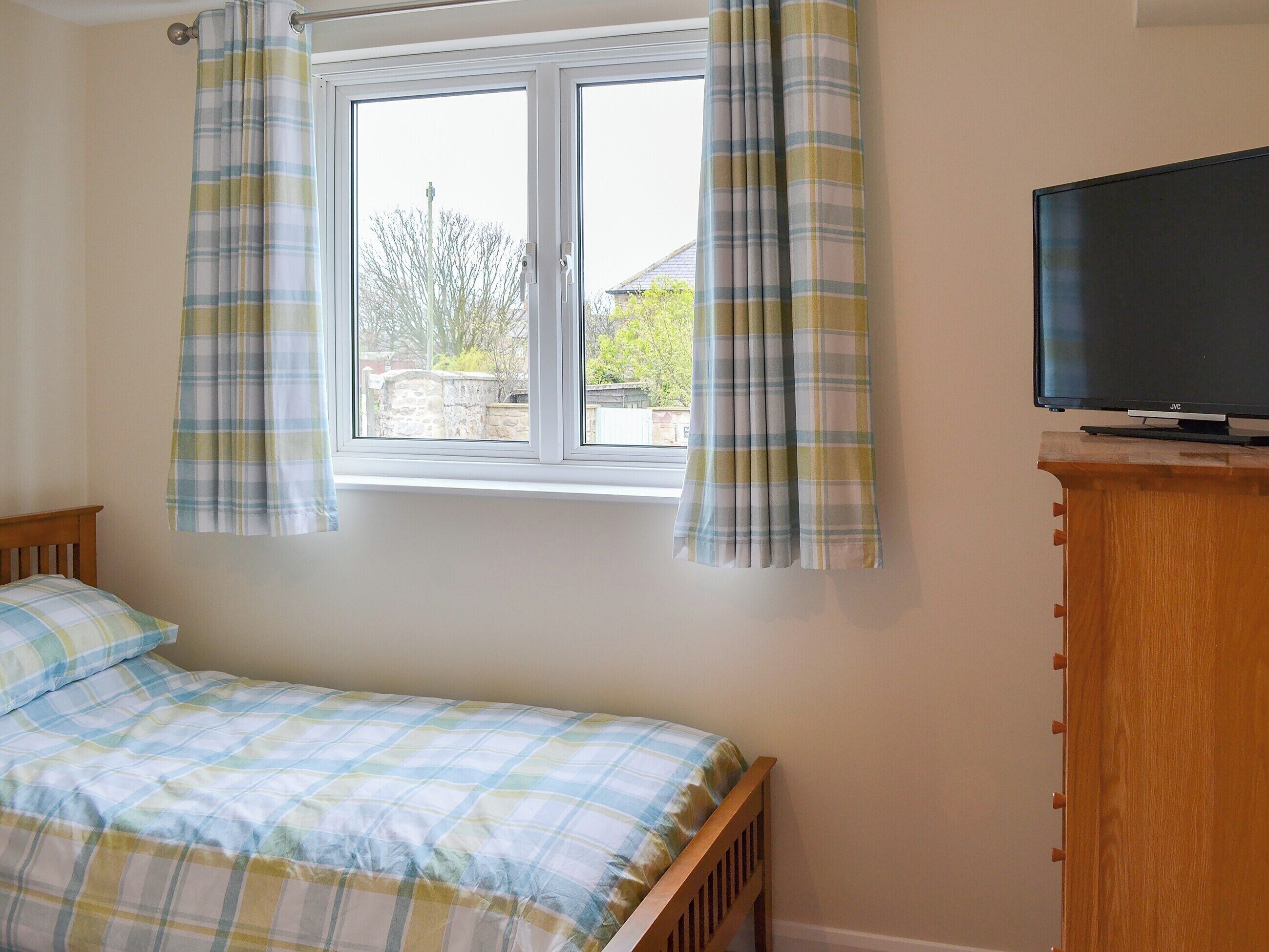 A bedroom with a bed, a window with curtains, and a television on a wooden stand.