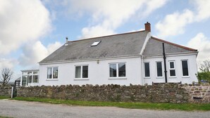 Une maison blanche à deux étages, avec des fondations en pierre, de nombreuses fenêtres et un toit en pente.
