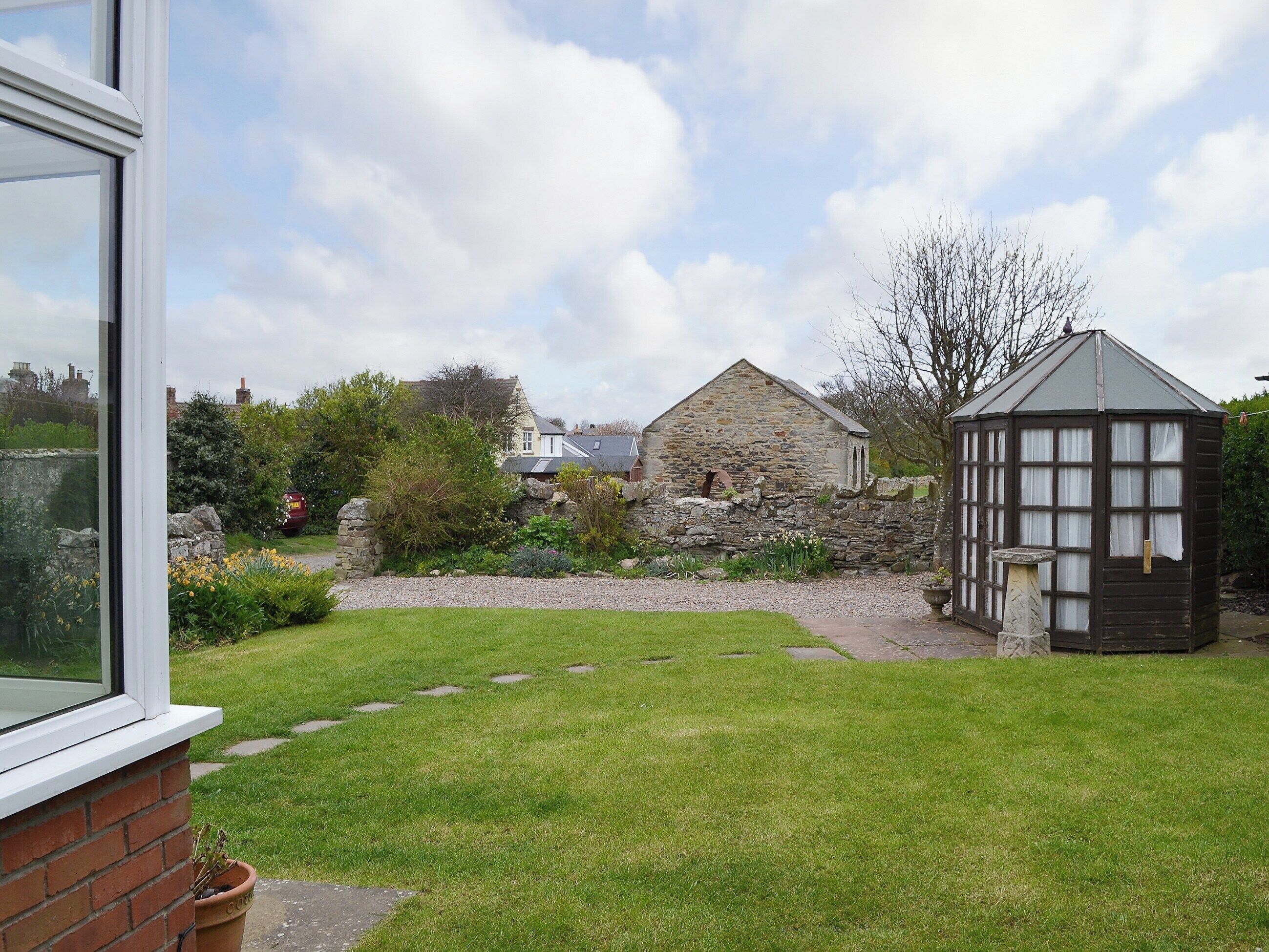 A garden with a stone building, a wooden structure, and a brick wall.