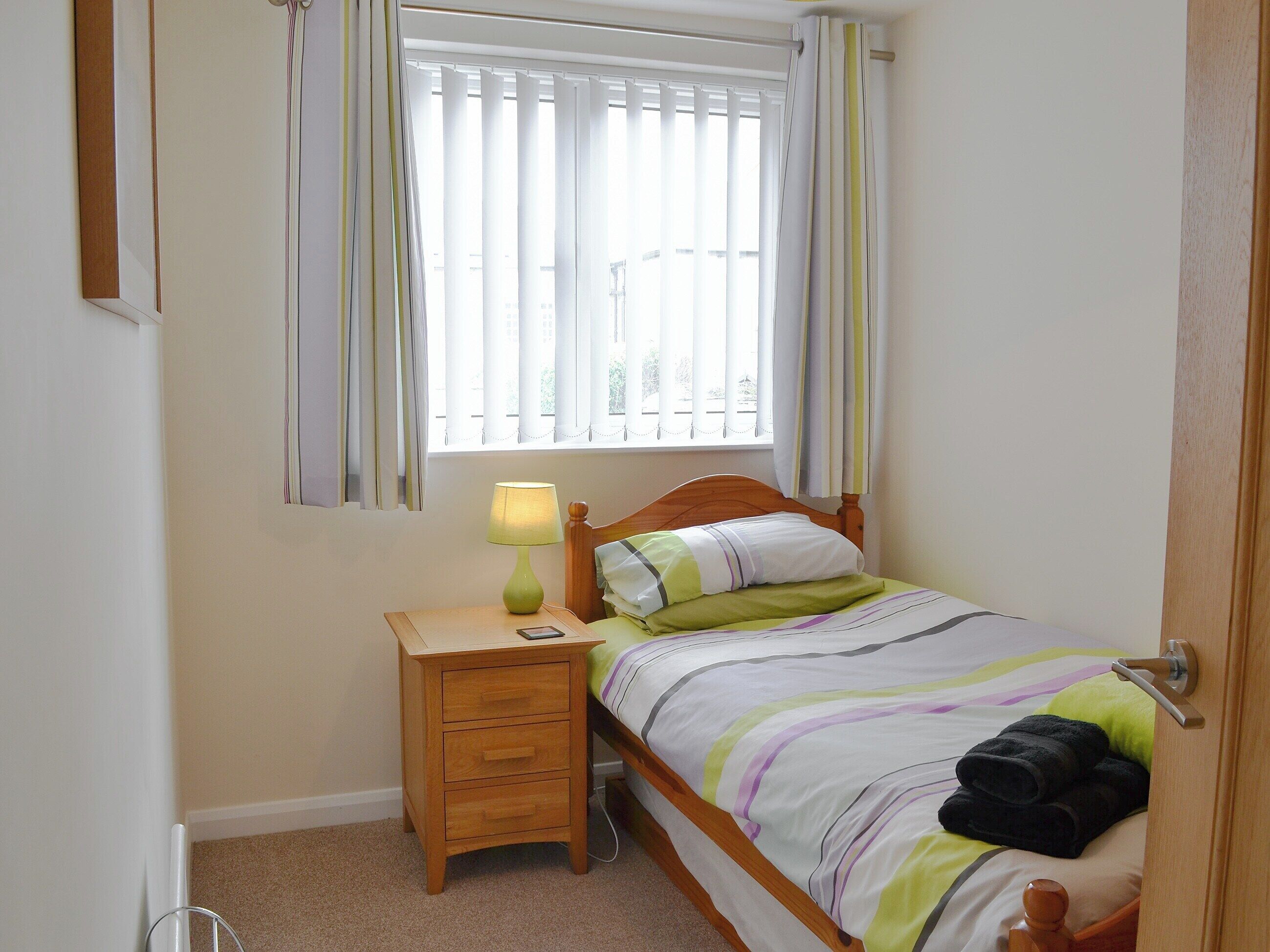 A bedroom with a bed, a nightstand, a lamp, and a window with curtains.