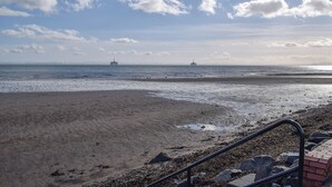 En strand med en pir i fjärran, en stenig kustlinje och ett metallräcke.