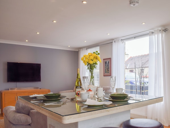 A modern kitchen with a central island, a flat-screen TV mounted on the wall, and a window with curtains.