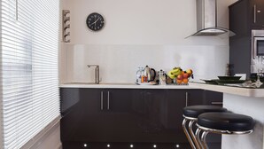 Ett modernt kök med en diskho i rostfritt stål, en klocka och en fruktskål på bänkskivan.