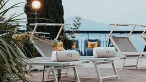 Un área al lado de la piscina con sillones de descanso, algunos con toallas, y un árbol grande al fondo.
