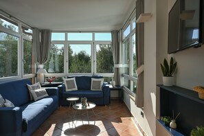 A sunlit room with a blue sofa, a small round table, and a TV mounted on the wall. - VillaBiancaSorrento-Sea View-Private Pool-Heated Jacuzzi-Gym-Private Car Park (Sorrento)