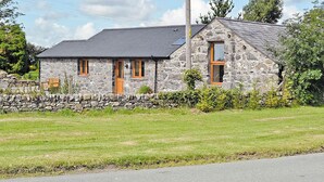 A stone house with a sloped roof, a wooden door, and a window. - Single storey barn conversion just a mile from a sandy beach. (Criccieth)