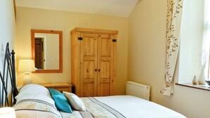 A bedroom with a bed, a nightstand, a dresser, a mirror, and a window with curtains. - Single storey barn conversion just a mile from a sandy beach. (Criccieth)