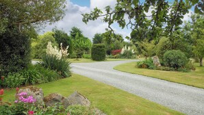 A gravel driveway curving through a well-maintained garden with various plants and flowers. - Single storey barn conversion just a mile from a sandy beach. (Criccieth)