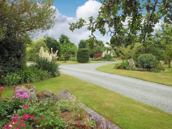 A gravel driveway curving through a well-maintained garden with various plants and flowers.
