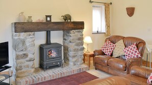 A cozy living room with a stone fireplace, leather sofa, and a television. - Single storey barn conversion just a mile from a sandy beach. (Criccieth)