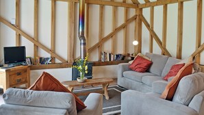 Ett mysigt vardagsrum med en öppen spis, synliga träbjälkar, en soffa, ett soffbord och en bokhylla.