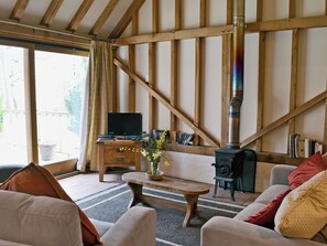 Un salon chaleureux avec une cheminée, des poutres apparentes, un téléviseur et une bibliothèque.