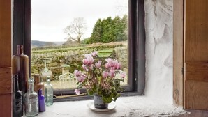 A window with a view of a stone wall and greenery, a potted plant with pink flowers, and several glass bottles on the windowsill. - THE OLD SHEAF STORE - KYZ (Glaisdale, near Whitby)