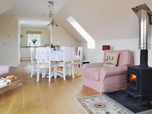 A cozy living room with a dining area, a pink sofa, a fireplace, and a kitchen in the background.