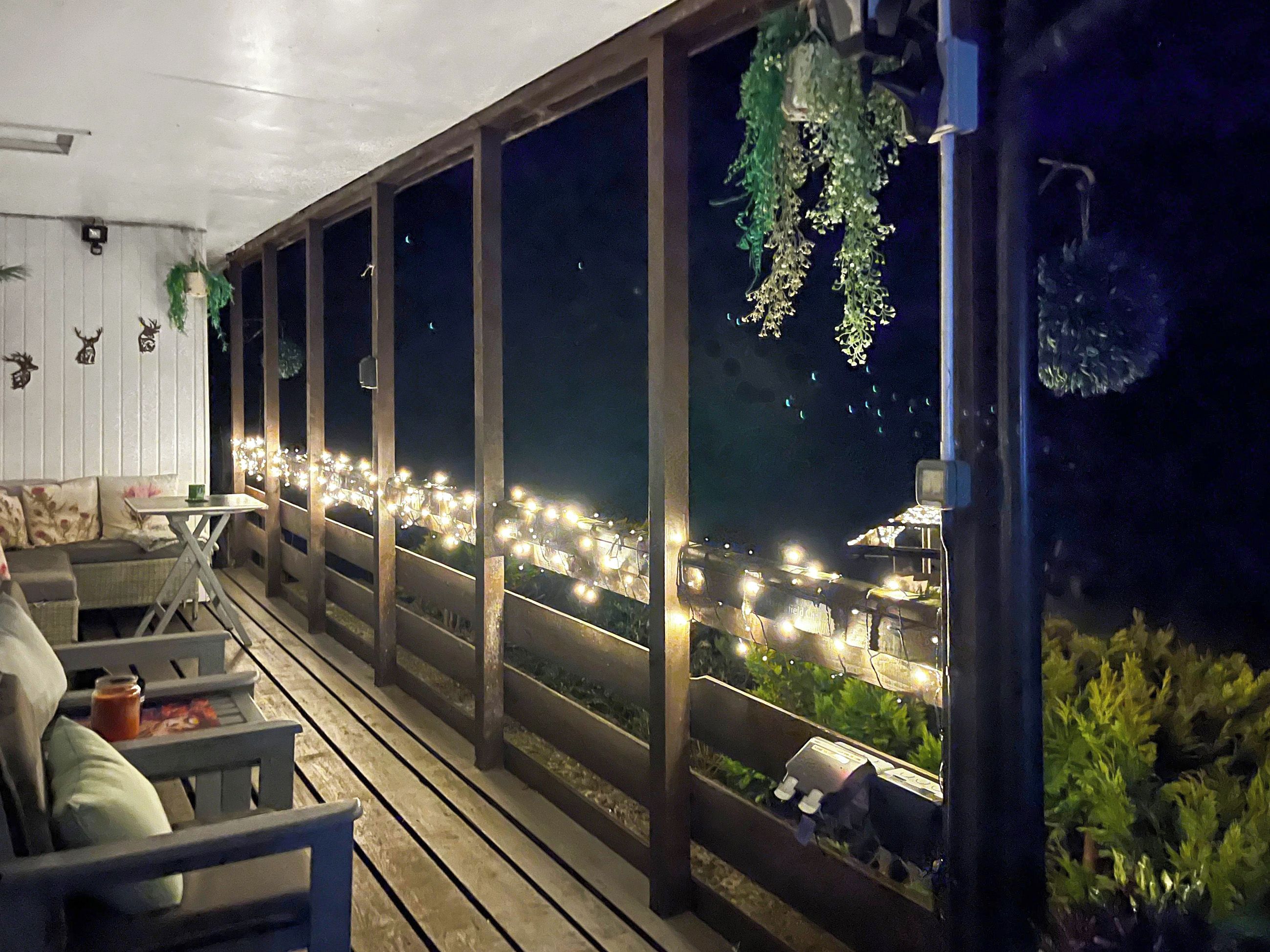 Un espace extérieur aménagé, abrité et doté de sièges, offrant une vue sur la ville la nuit, avec des bancs en bois et une table sur laquelle se trouve une boisson.