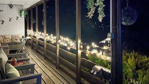 A covered outdoor seating area with a view of the city at night, wooden benches, and a table with a drink. - 2 bedroom accommodation in Lanark (Lanark)