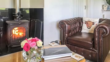 En stue med en lædersofa, et glasbord, en vase med blomster, en bog og en brændeovn.
