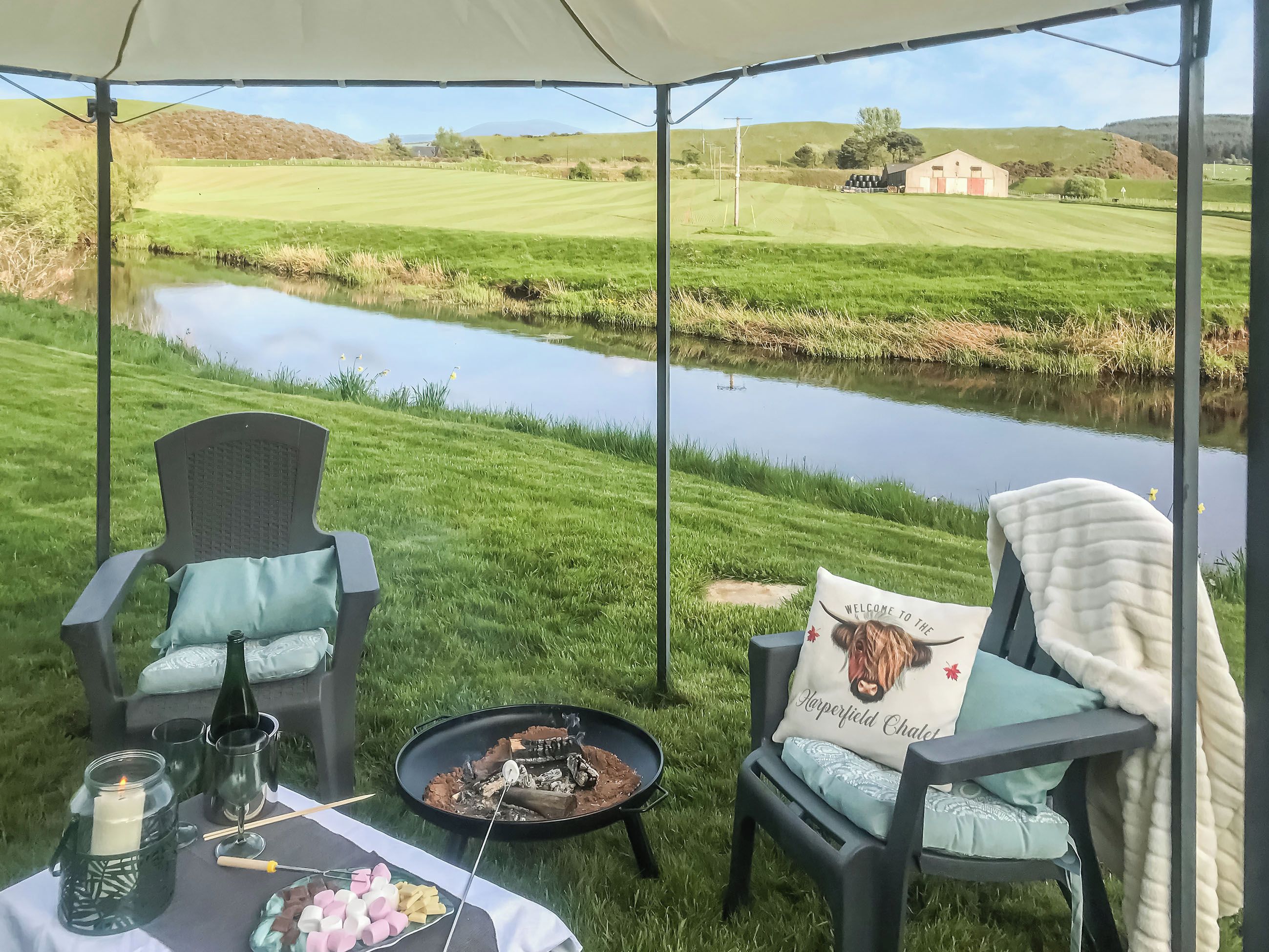 Un espacio al aire libre con carpas, sillas, una mesa con aperitivos, una vela y una chimenea.