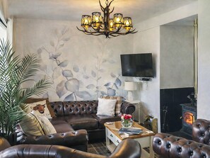 A living room with a fireplace, a television mounted on the wall, and a chandelier. - 2 bedroom accommodation in Lanark (Lanark)