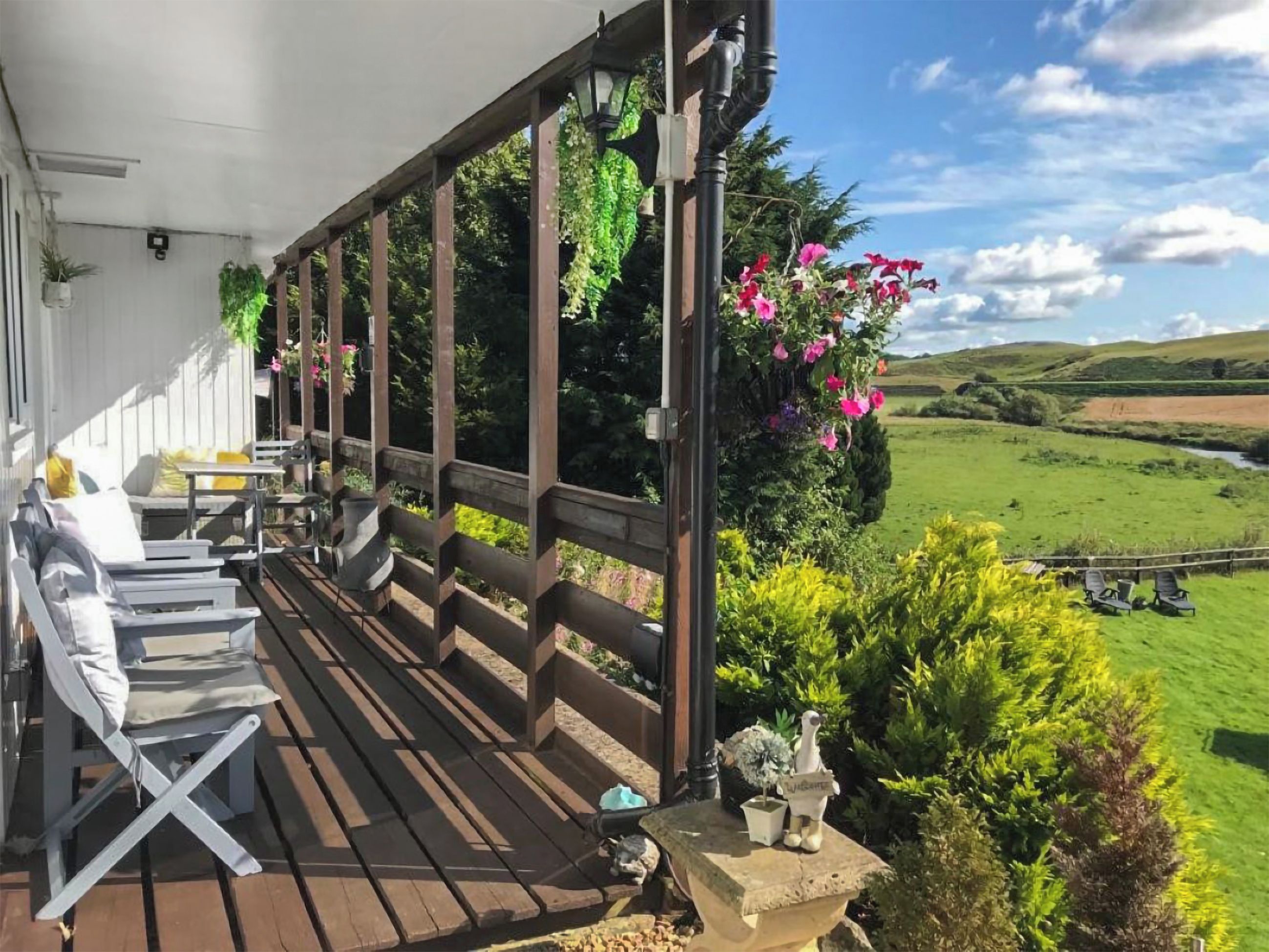 Una terraza de madera con asientos al aire libre, una jardinera de piedra con una estatua y vistas a un paisaje verde.