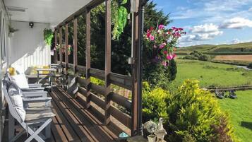Una terraza de madera con asientos al aire libre, una jardinera de piedra con una estatua y vistas a un paisaje verde.